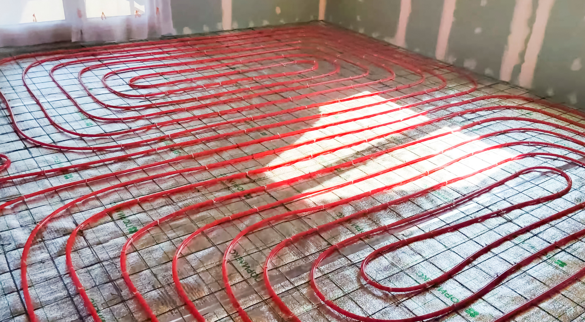 Tuberías de calefacción por suelo radiante de color rojo instaladas sobre rejilla, preparadas para suelo de hormigón.