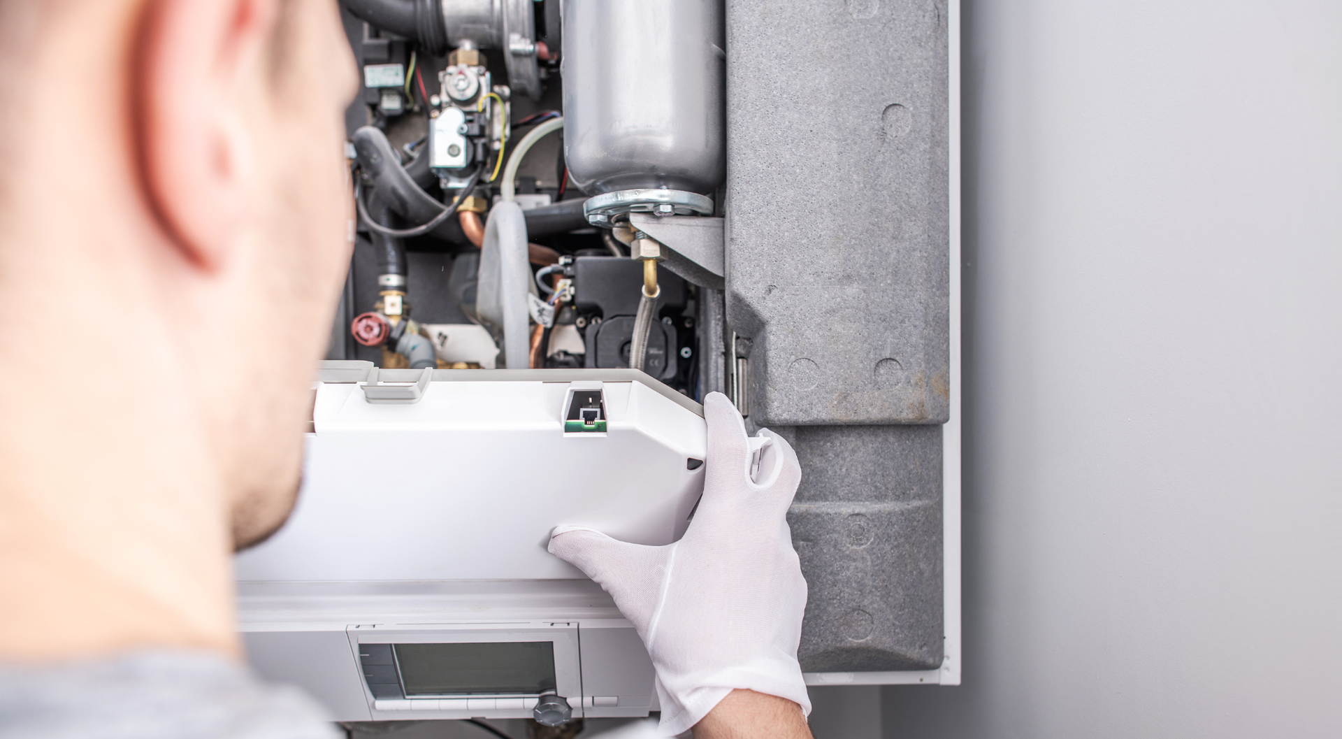 Persona con guantes trabajando en una unidad de calefacción blanca, quitando un panel.