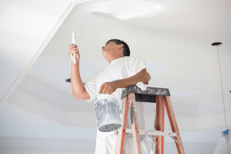 Pintor en una escalera de mano, pintando un techo blanco.