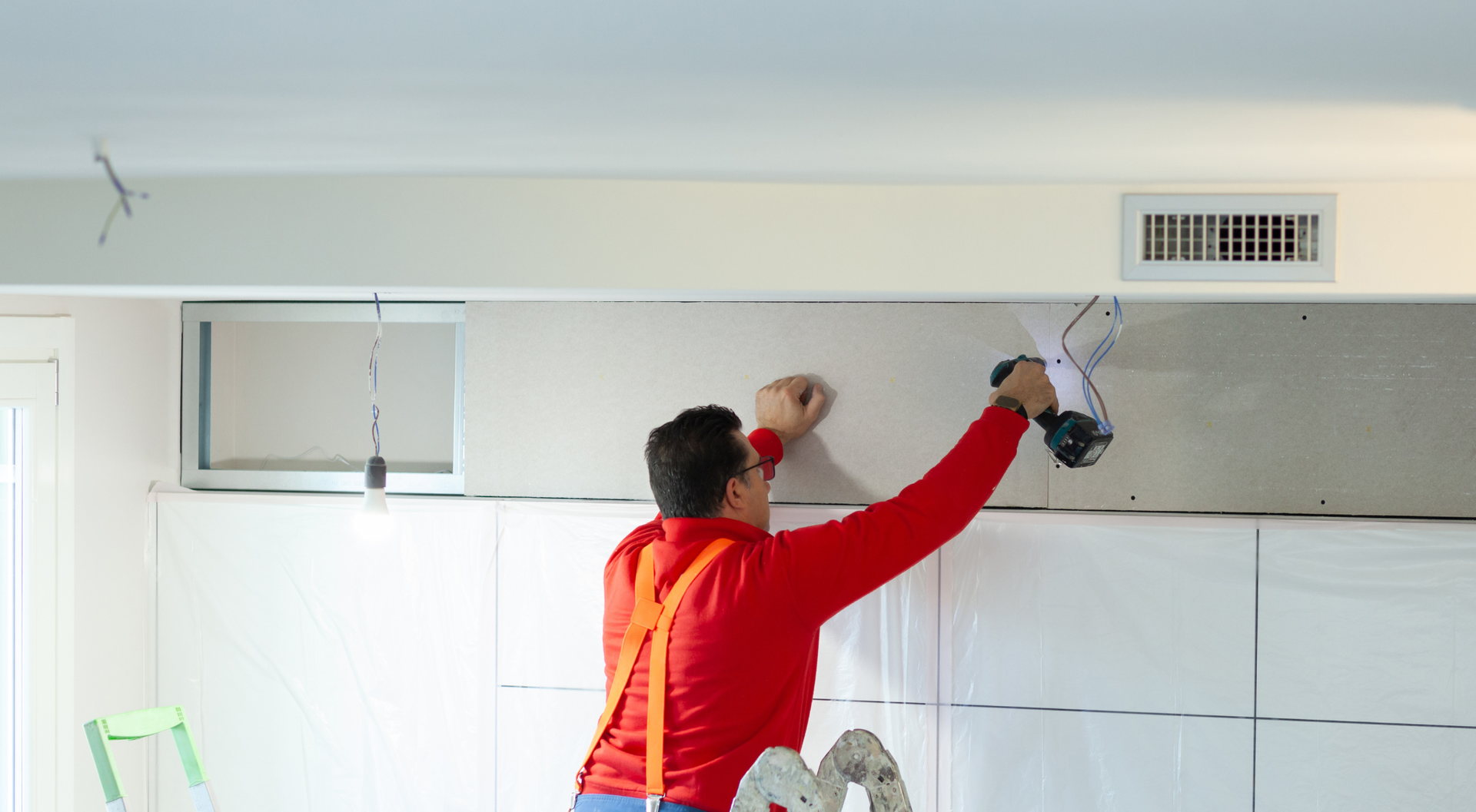 Persona con camisa roja instalando paneles de yeso en una pared cerca de un respiradero del techo.