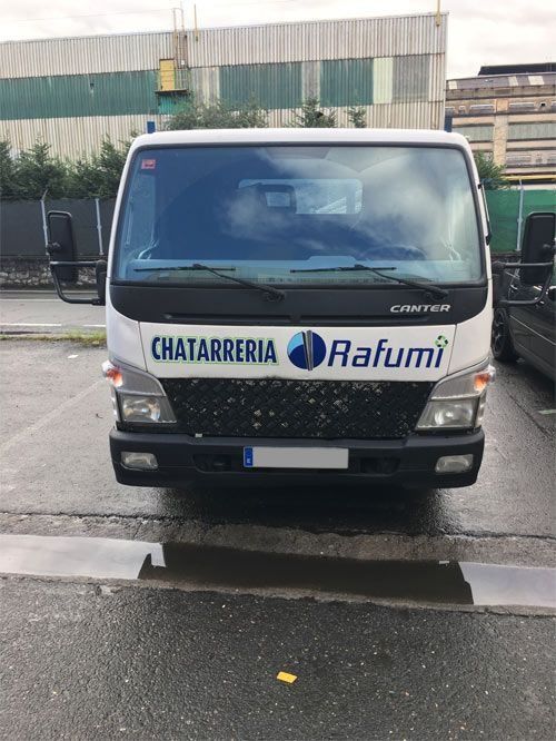 Camioneta de reparto blanca con el logotipo de “Chatarreria Rafumi” estacionada en una calle mojada frente a un edificio.