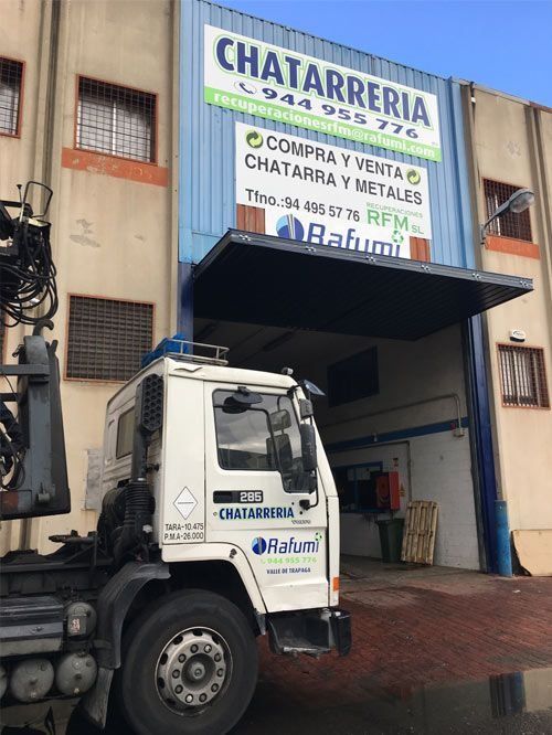 Camioneta blanca estacionada junto a una tienda con un gran letrero de “CHATARRERIA” y un toldo azul.