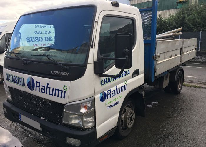Camión de reparto blanco de Raufmi estacionado al aire libre en una calle mojada, vista lateral.