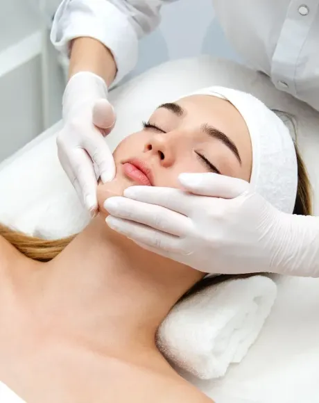 Mujer recibiendo tratamiento facial; manos con guantes en la cara.