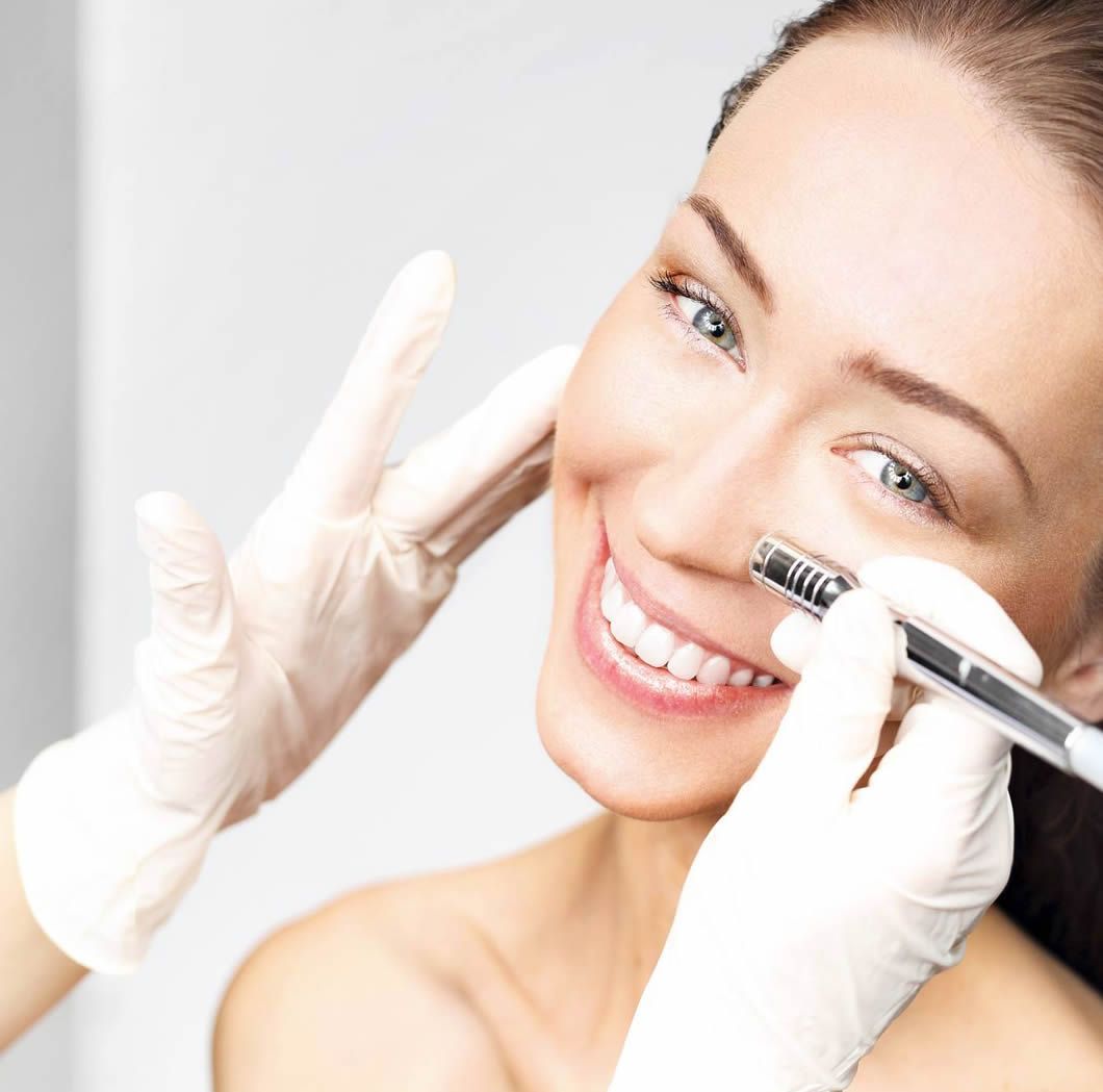 Mujer recibiendo un tratamiento facial con manos enguantadas, sonriendo.
