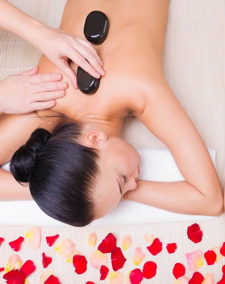 Mujer recibiendo masaje con piedras calientes en la espalda, con pétalos de rosa esparcidos.