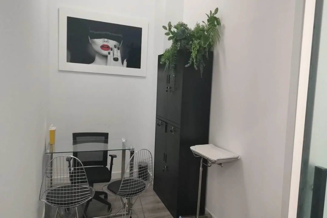 Un espacio de salón con un armario negro, un escritorio y una foto en la pared, y vegetación encima.