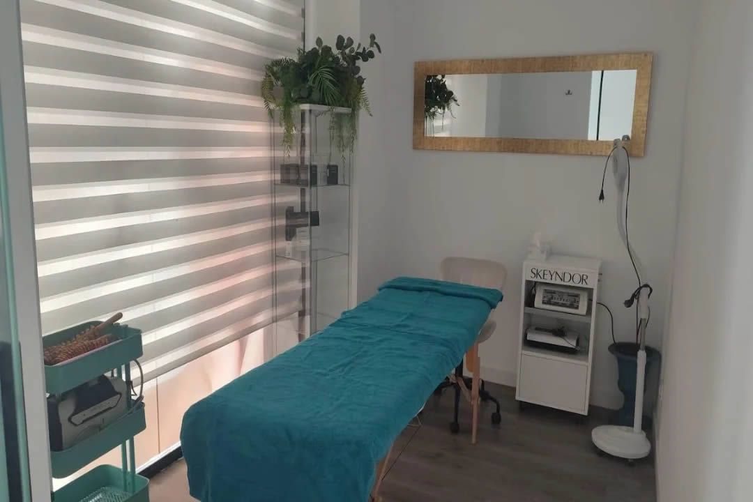 Sala de tratamientos de spa con cama verde azulado, espejo y equipamiento.