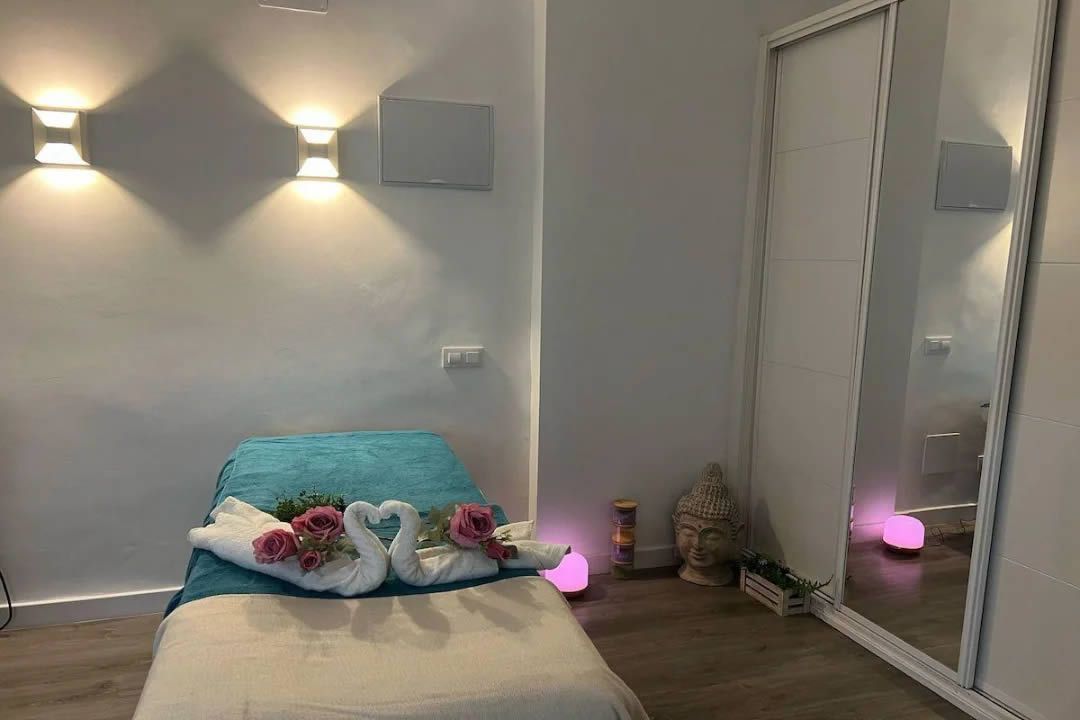 Sala de masajes con camilla, cisnes de toallas e iluminación.