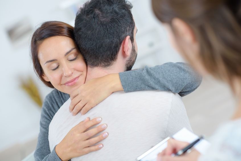 Mujer abrazando a una persona durante una sesión de terapia, con un bloc de notas visible en primer plano.