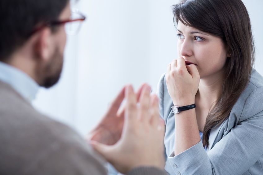 Dos personas conversando al otro lado de una mesa, una gesticulando mientras la otra escucha con expresión preocupada.