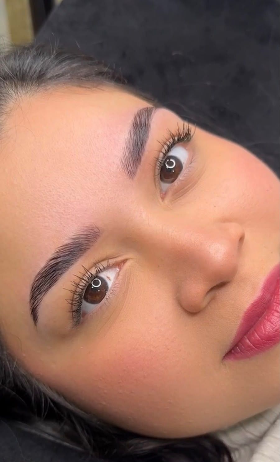 Primer plano del rostro de una mujer con maquillaje natural, cejas oscuras y lápiz labial rosa, mirando a la cámara.