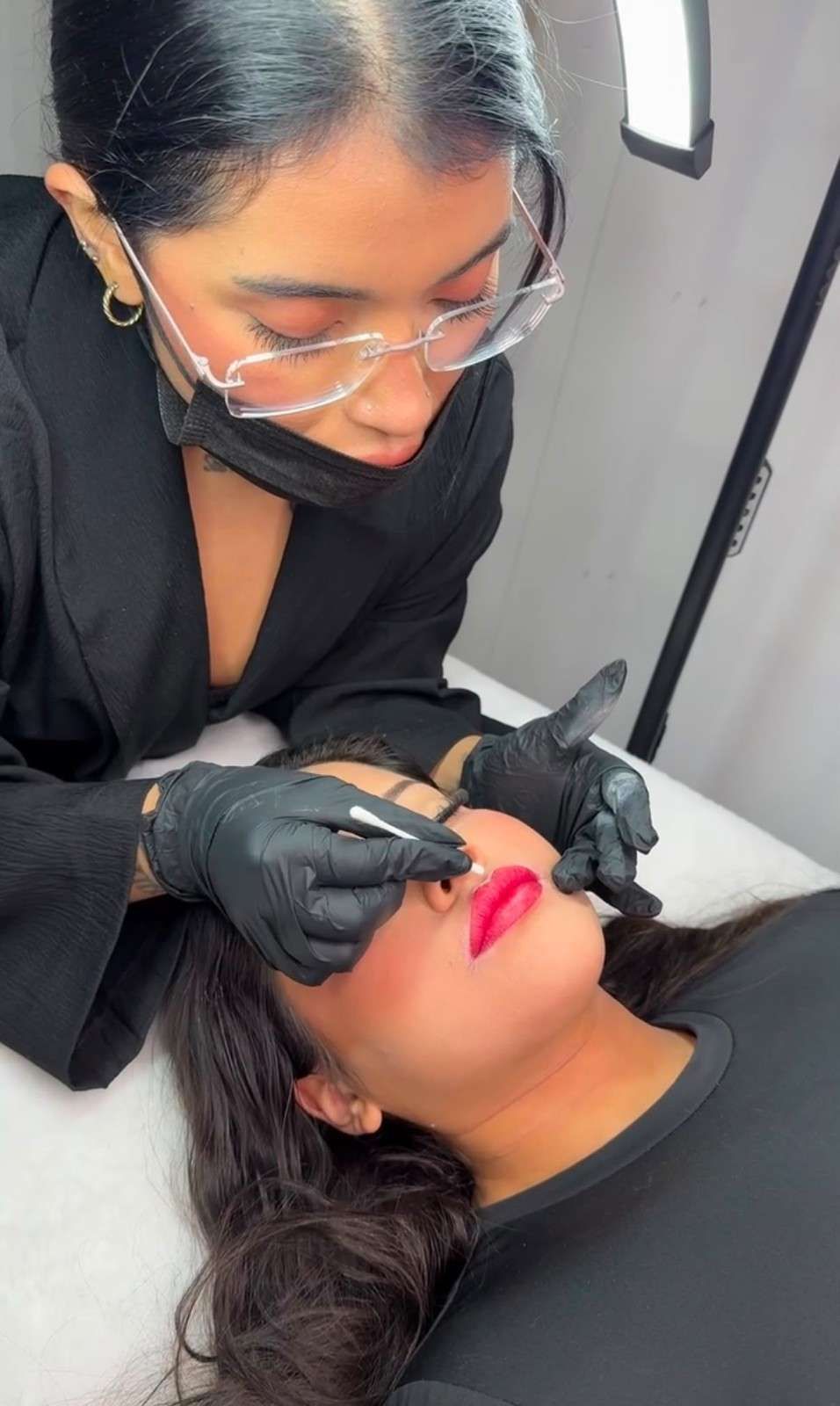 Técnica aplicando tratamiento labial a una clienta con gafas protectoras y guantes negros en el interior.