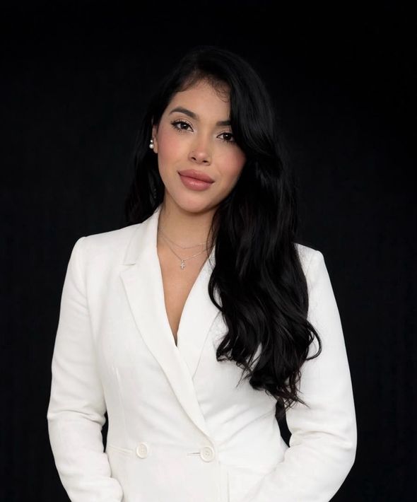 Retrato de una mujer con un blazer blanco sobre fondo negro, mirando al frente con una leve sonrisa.