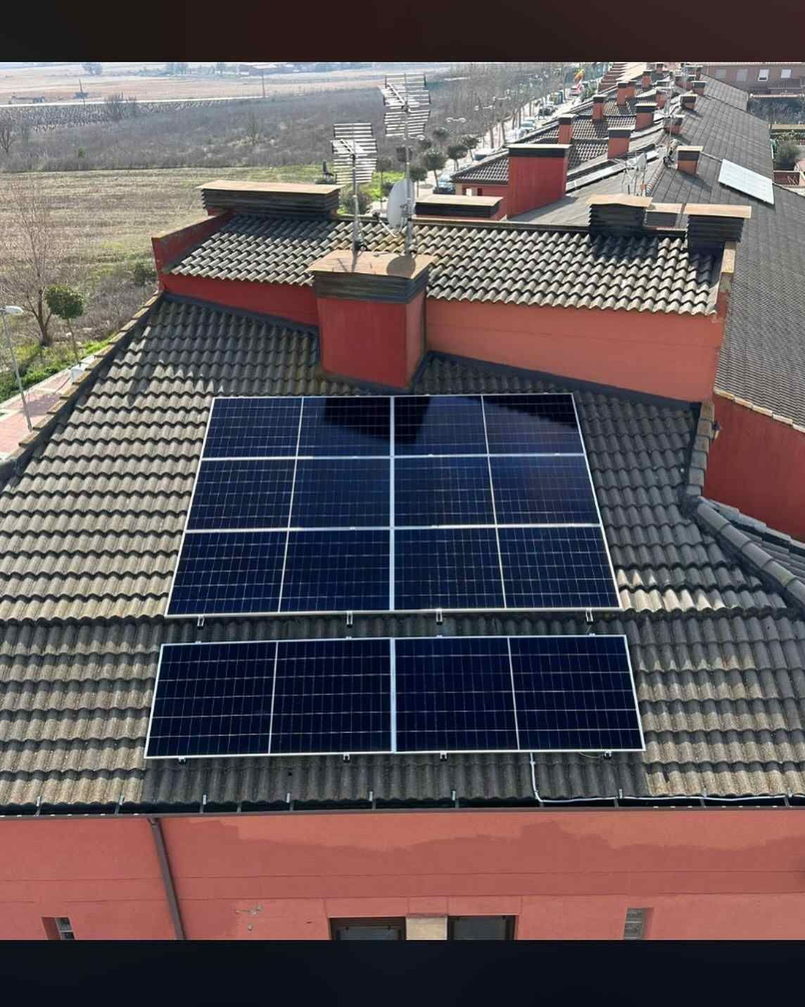 Azotea con dos filas de paneles solares en edificios con tejados de tejas rojas bajo un cielo nublado