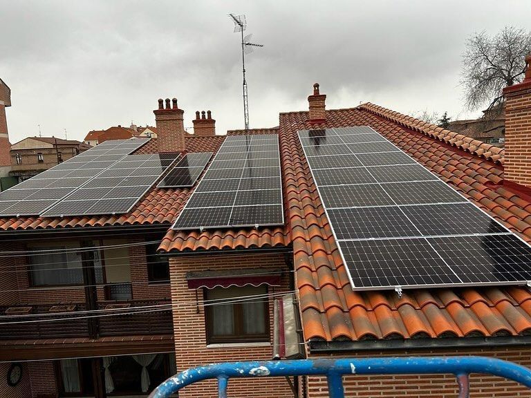 Tejados de casas con tejas rojas y varios conjuntos de paneles solares bajo un cielo nublado