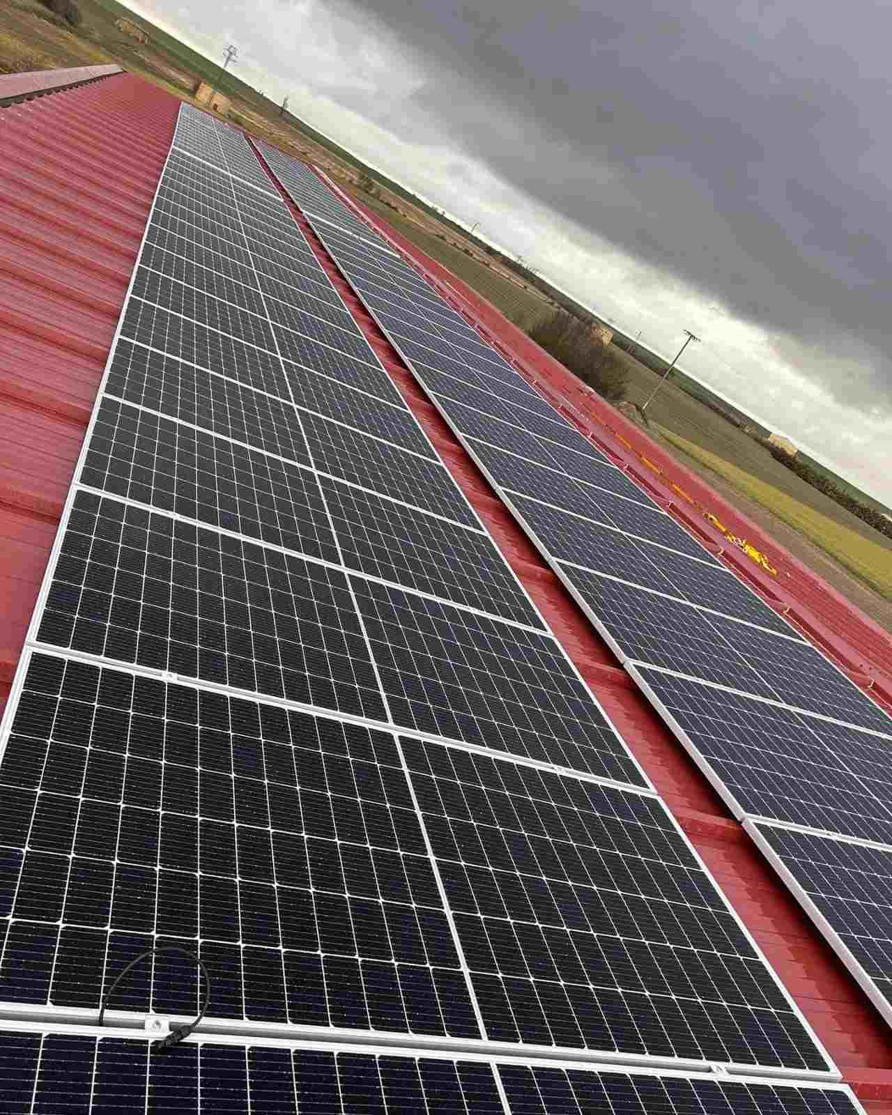 Filas de paneles solares oscuros sobre un tejado rojo bajo un cielo nublado