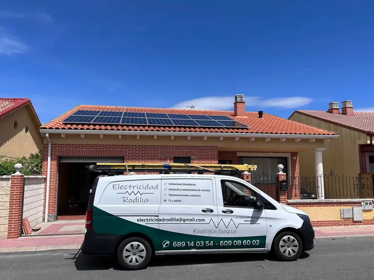 Furgoneta blanca de servicios estacionada frente a una casa con paneles solares bajo un cielo azul despejado