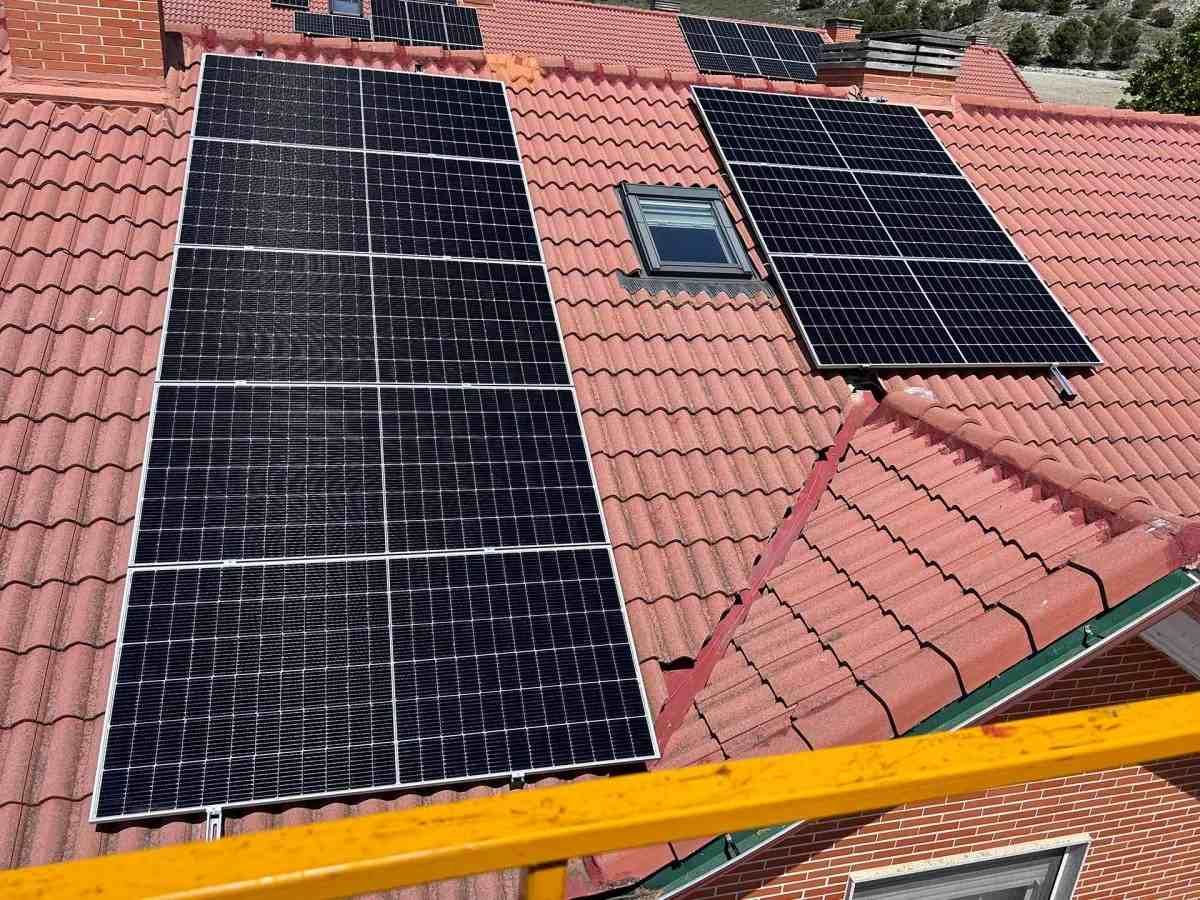 Tejado con tres paneles solares instalados sobre tejas de barro rojo junto a una claraboya.