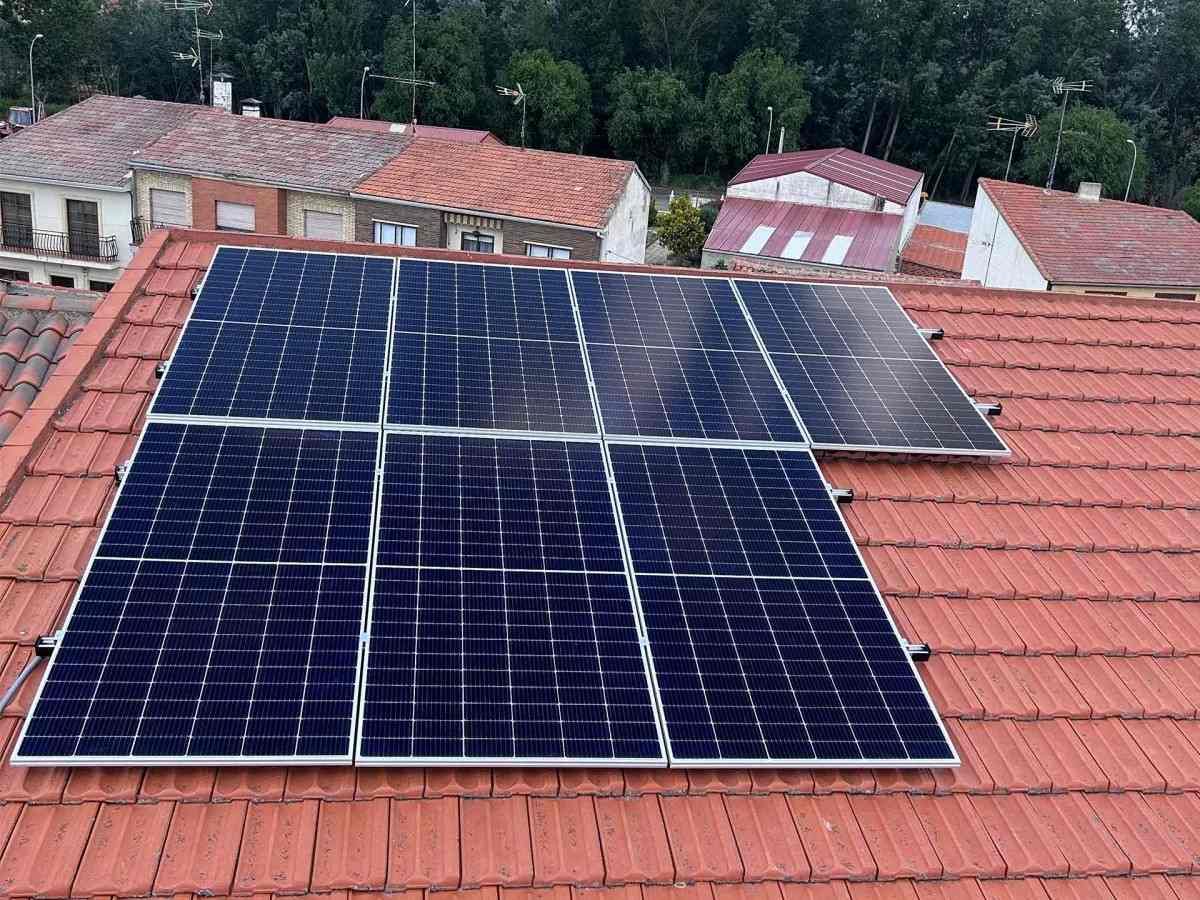 Paneles solares instalados en un tejado de tejas rojas, con casas y árboles al fondo
