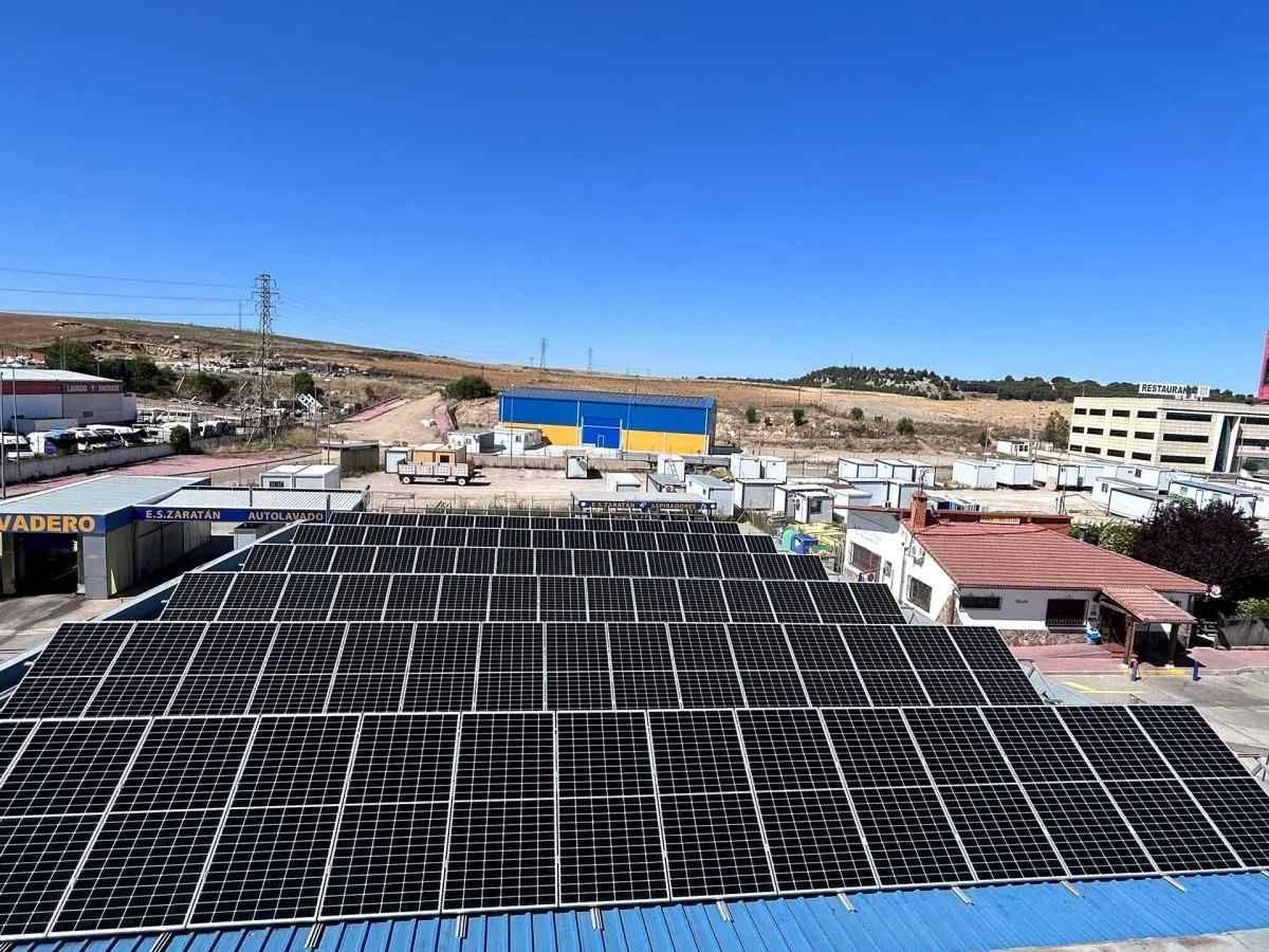 Instalación de paneles solares en la azotea bajo un cielo azul despejado, con edificios cercanos y una ladera al fondo