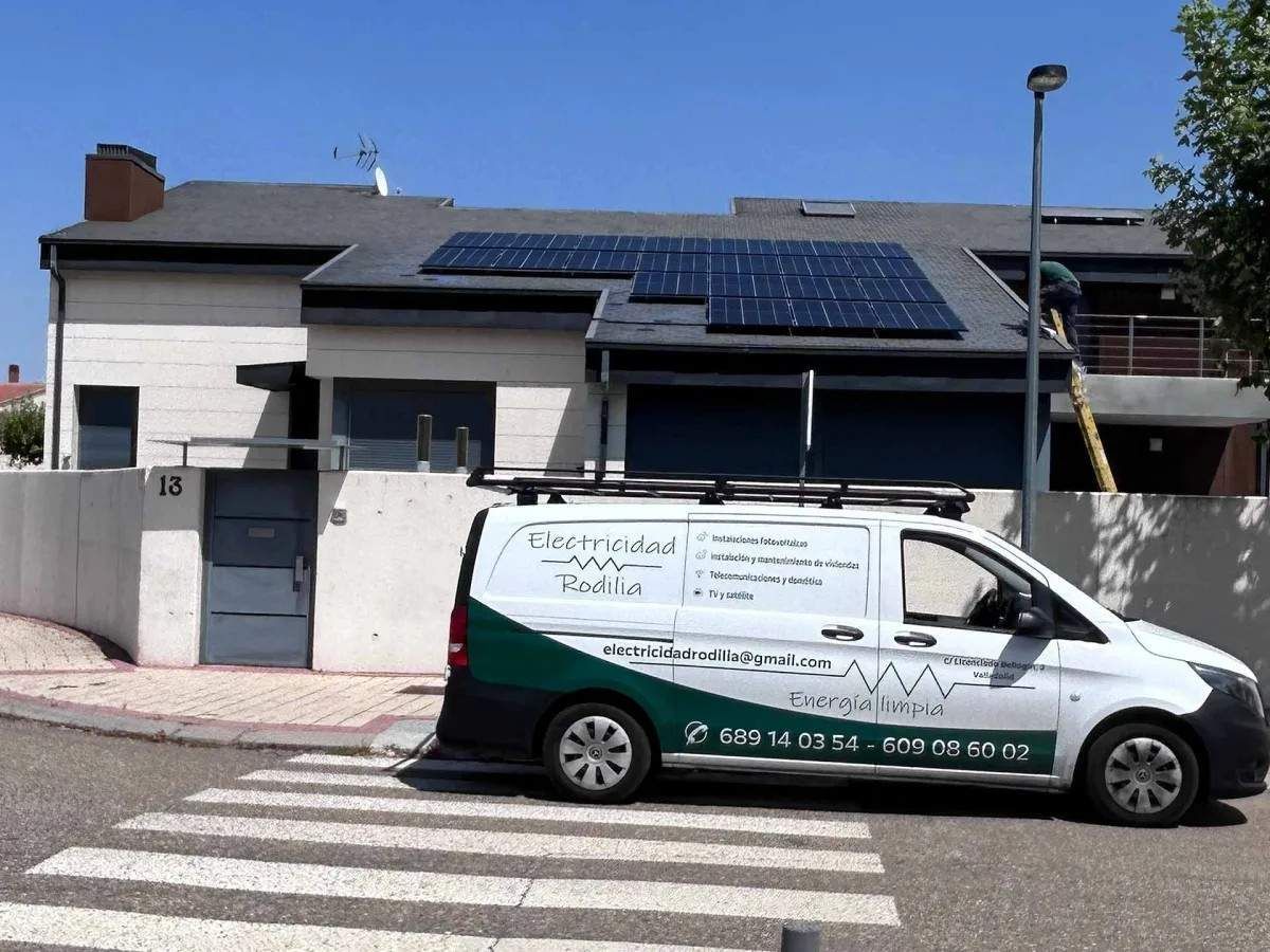 Furgoneta de servicio blanca y verde aparcada junto a un edificio con paneles solares, cerca de un paso de peatones.