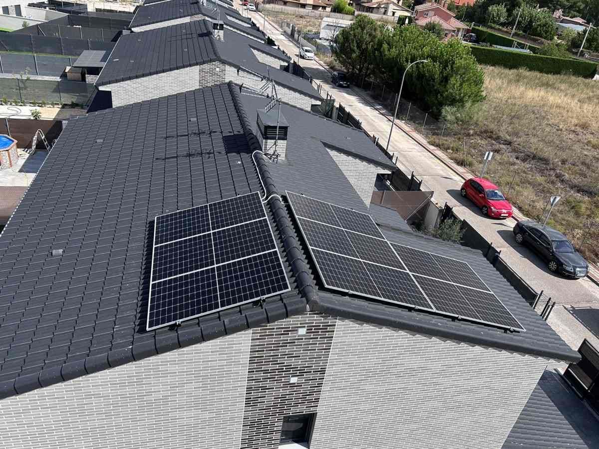 Casa con techo de tejas grises y paneles solares, junto a una carretera y varios coches aparcados