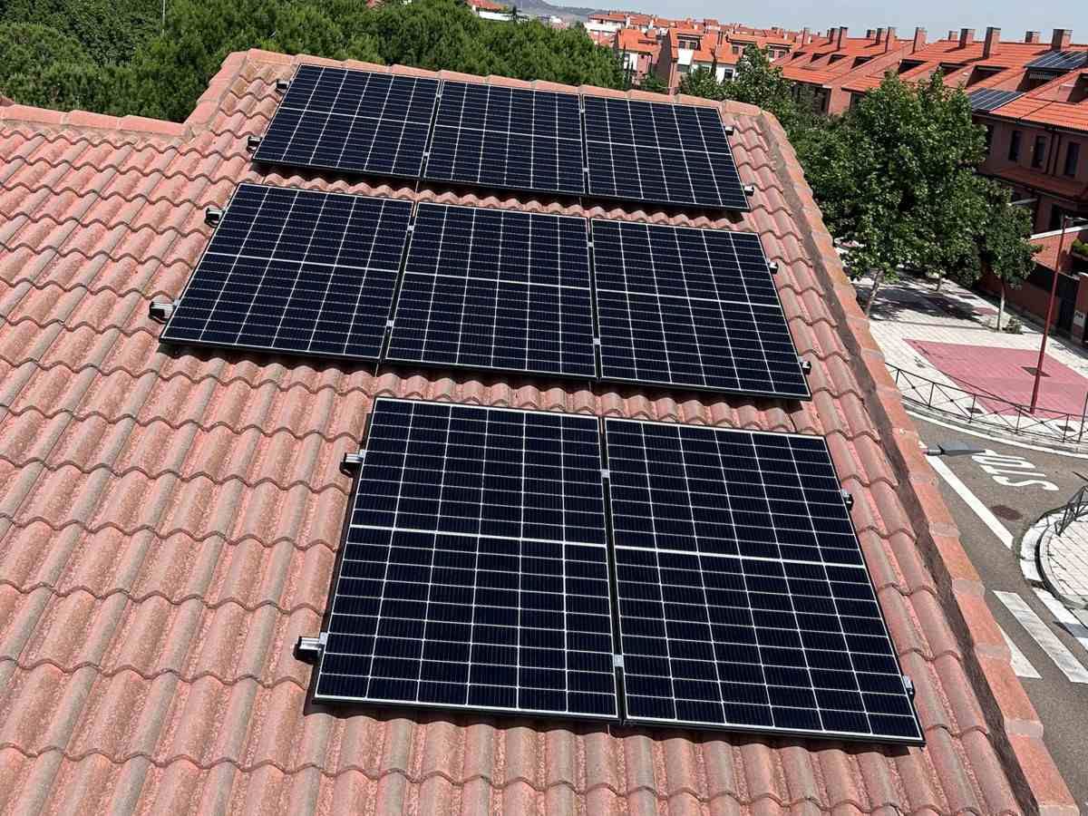 Tres paneles solares sobre un tejado de tejas de terracota, con un paisaje urbano al fondo