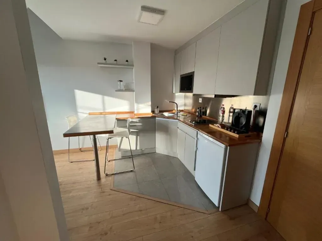 Pequeña cocina moderna con gabinetes blancos, encimera de madera, mesa de comedor y piso de madera clara.