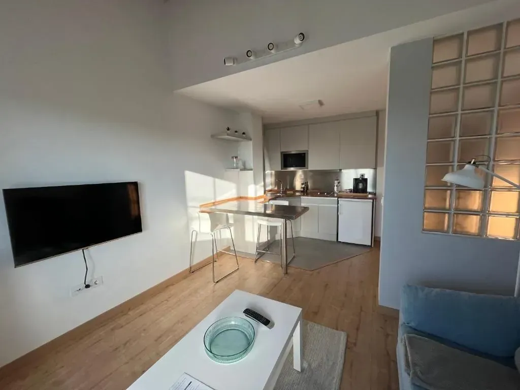 Dormitorio con pared de piedra blanca, vigas de madera, cama con ropa de cama blanca y almohadas decorativas.