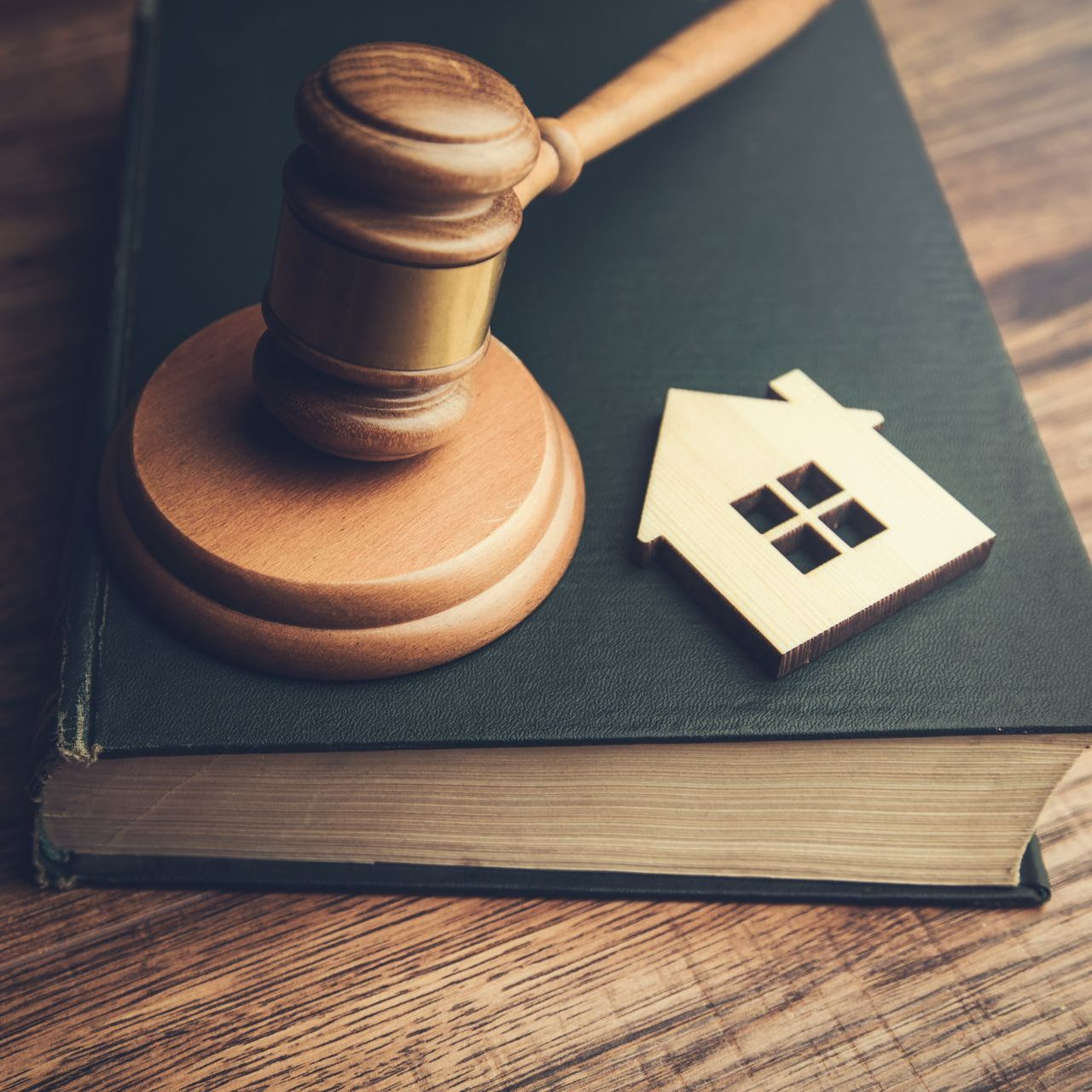 Petite maison en bois et marteau de juge placé sur un livre à couverture noire