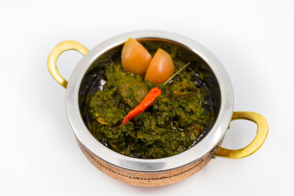 Un bol de curry vert garni de rondelles de carotte et d'un piment rouge, dans un plat de service en métal à poignées jaunes.