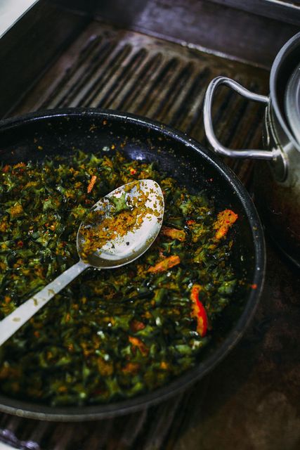 Une poêle contenant des légumes verts hachés, avec une cuillère à côté d'une casserole sur la plaque de cuisson.