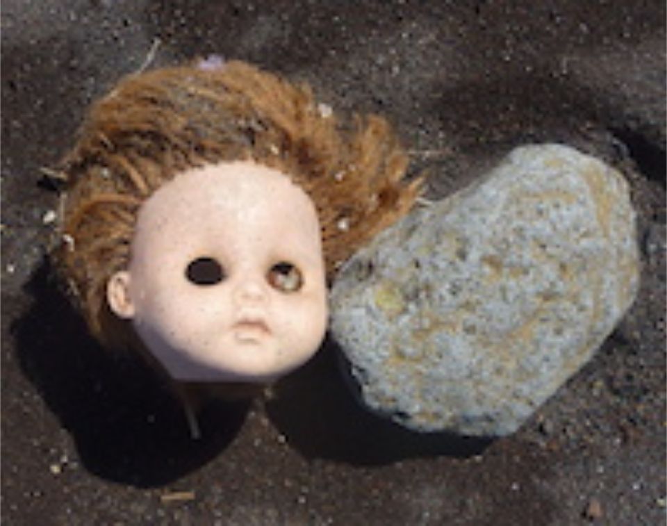 Puppenkopf ohne Augen neben Stein