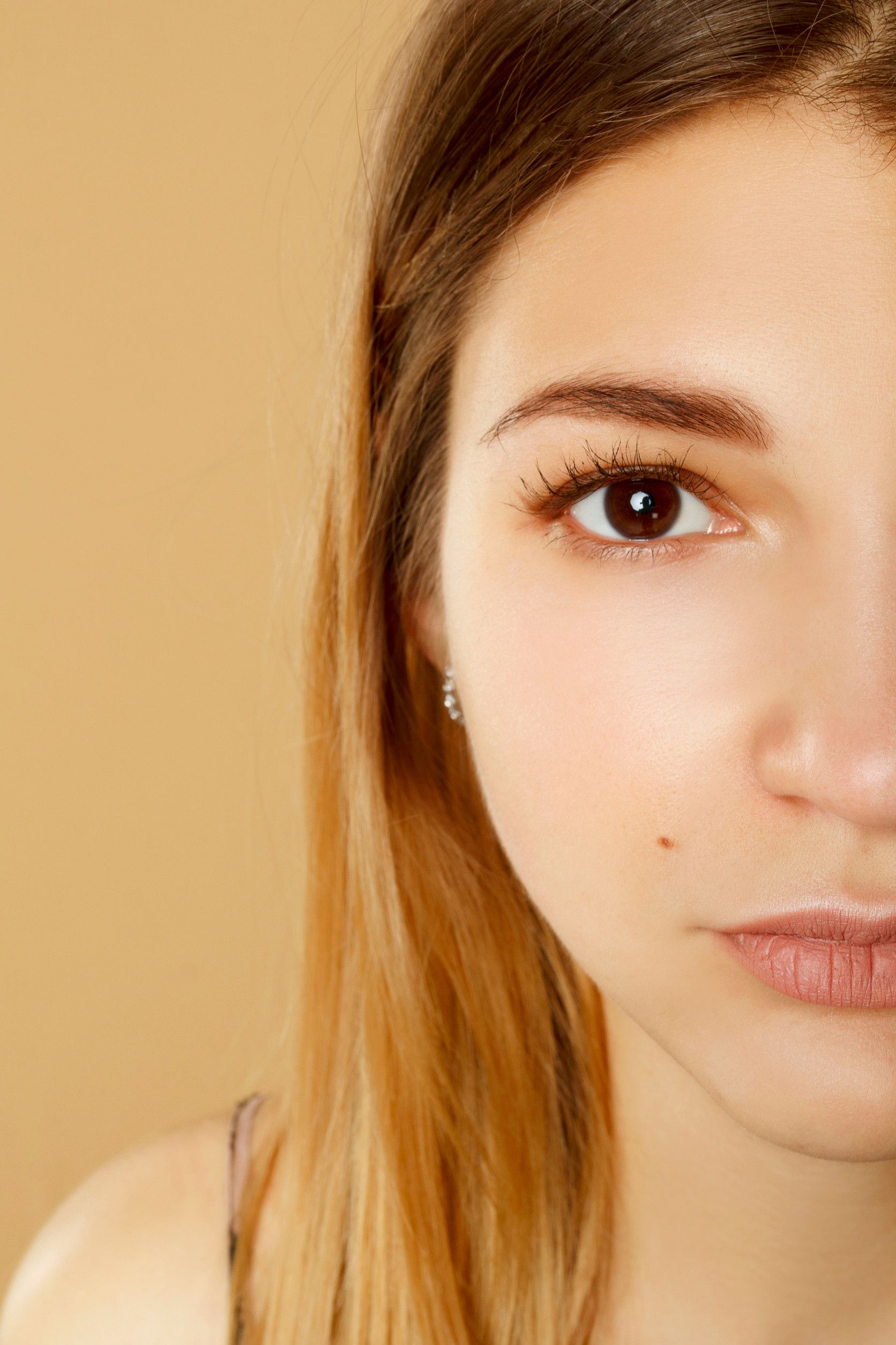 Primer plano del rostro de una mujer, de medio perfil. Piel clara, ojos marrones, cabello castaño claro, fondo neutro.