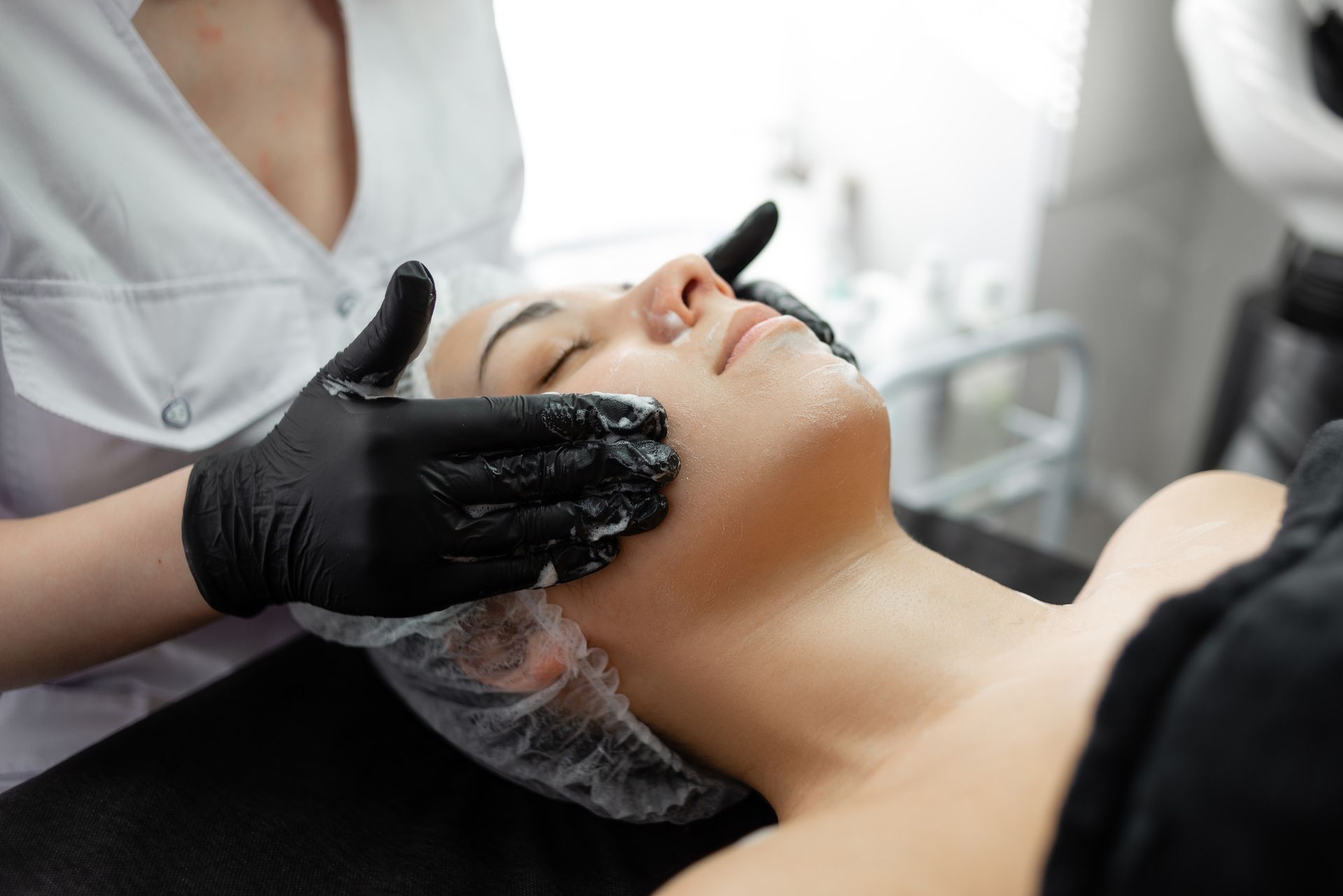 Mujer recibiendo tratamiento facial. Esteticista con guantes aplicando el producto. Interior.