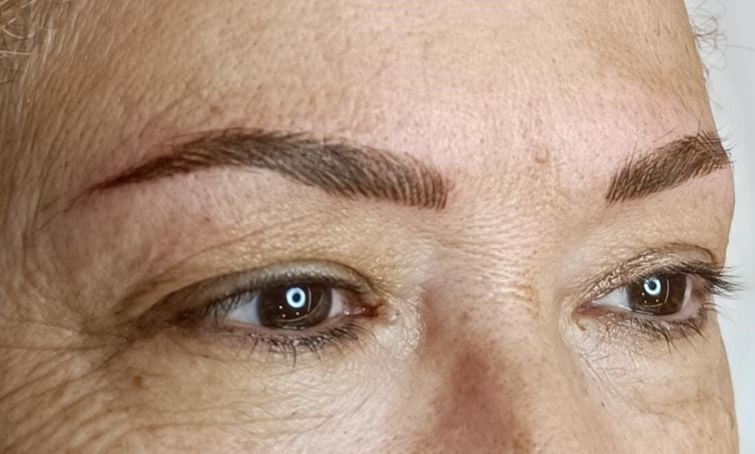 Rostro de mujer con cejas marrones microblading; ojos marrones, piel clara; iluminación natural.