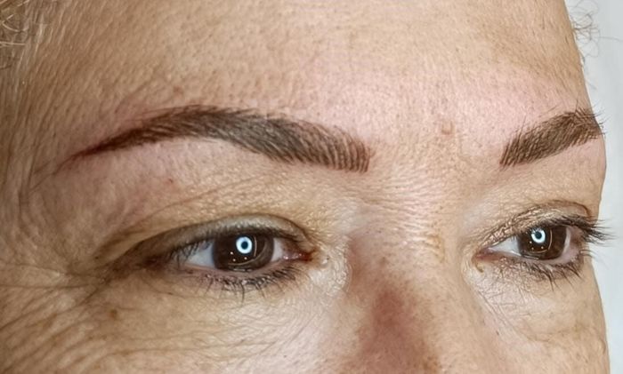 Rostro de mujer con cejas marrones microblading; ojos marrones, piel clara; iluminación natural.