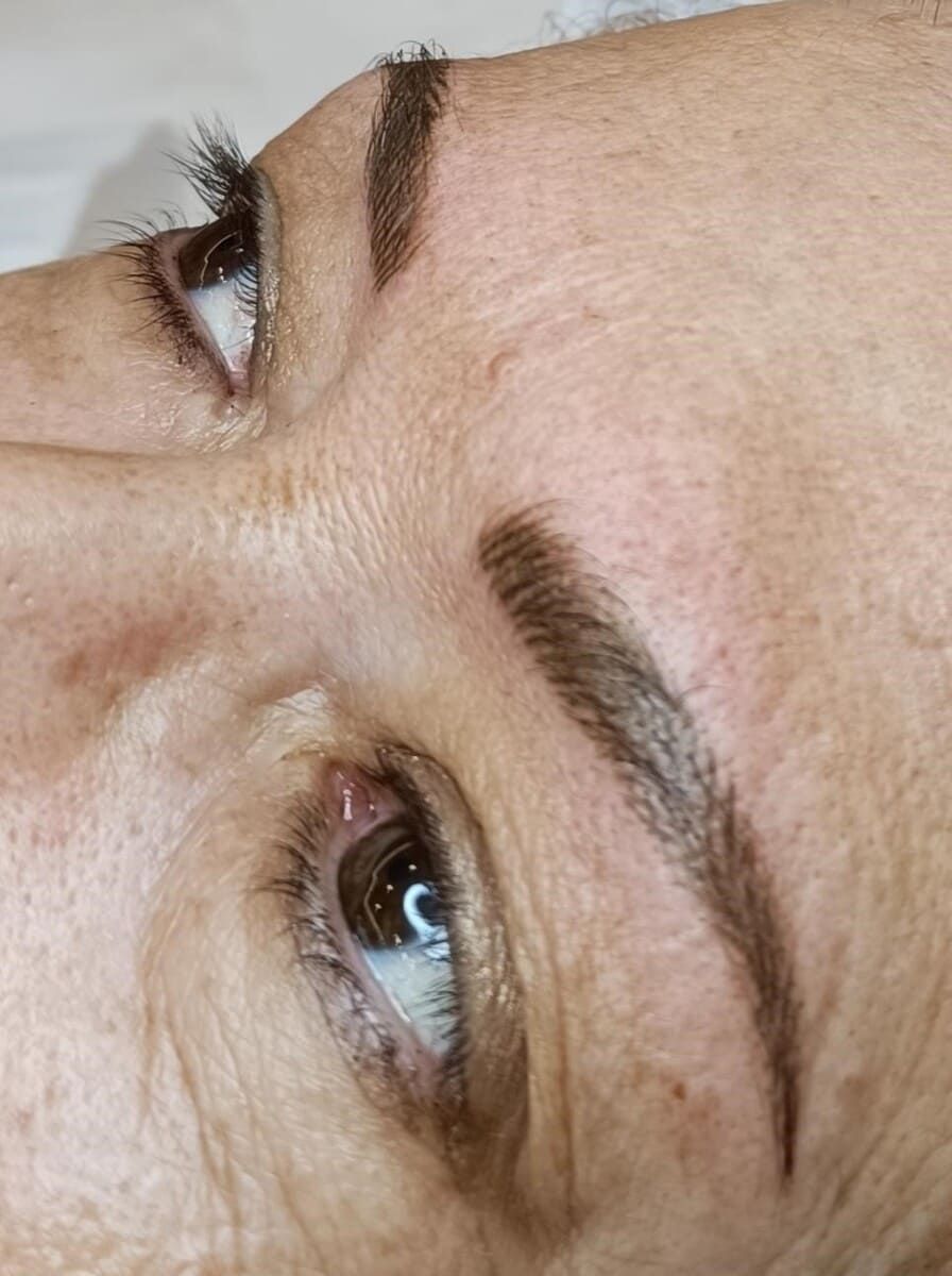 Primer plano del rostro de una persona, mostrando cejas realzadas con microblading. Pigmento marrón con trazos visibles.