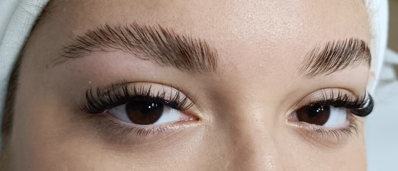 Primer plano del rostro de una persona con ojos marrones, pestañas oscuras y cejas recogidas.