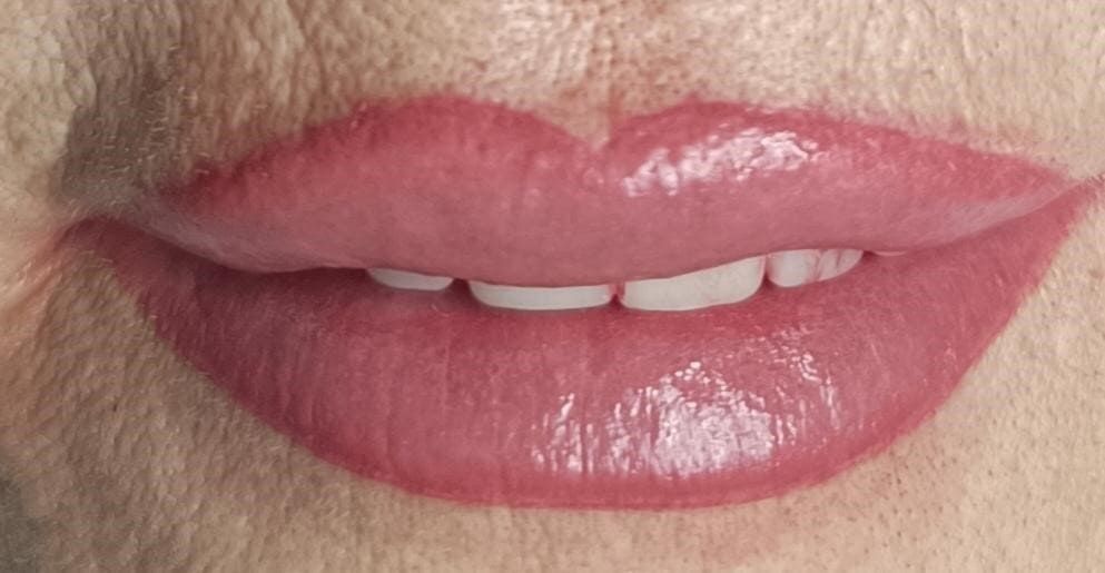 Primer plano de los labios rosados de una mujer, sonriendo levemente y mostrando los dientes blancos.