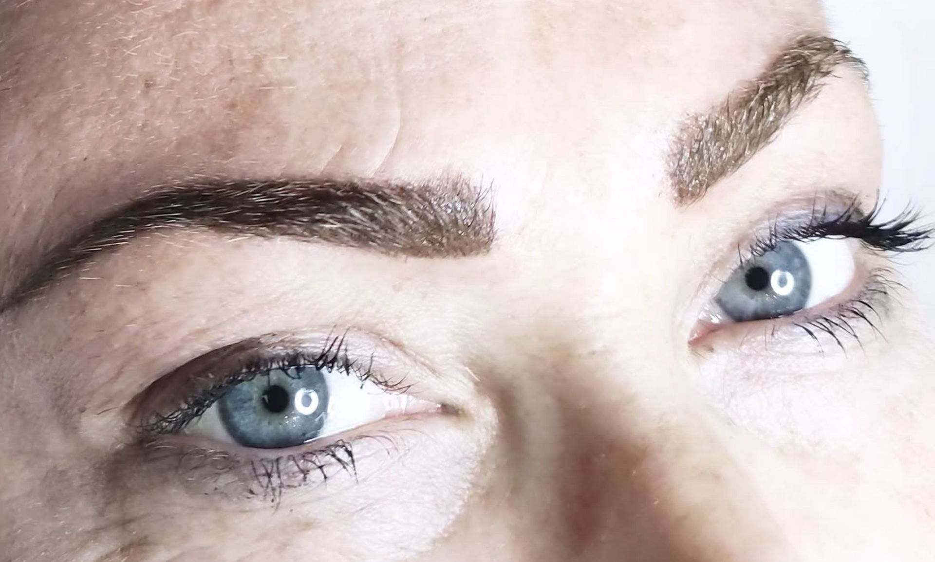 Primer plano de una mujer de piel clara, ojos azules y cejas de color marrón oscuro y bien definidas.