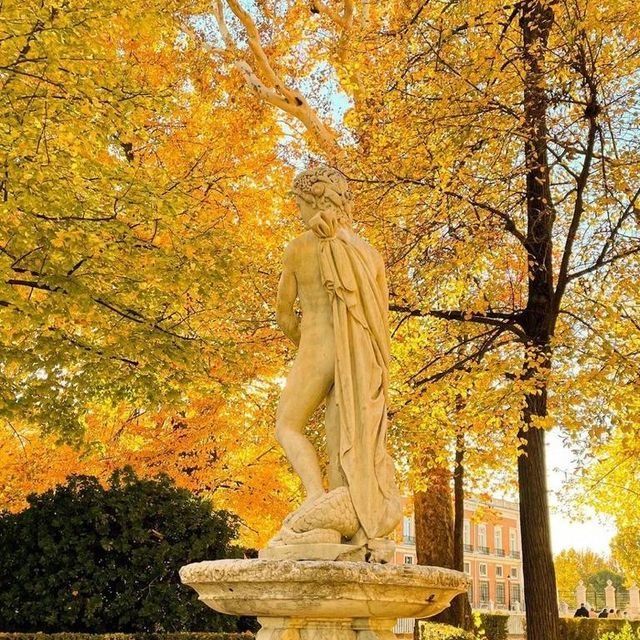 Una estatua de una mujer parada en una fuente frente a árboles con hojas amarillas.
