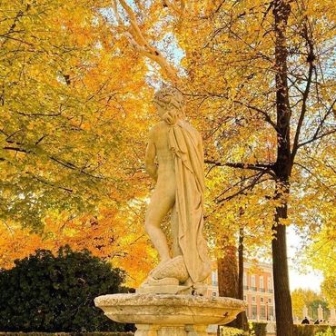 Una estatua de una mujer parada en una fuente frente a árboles con hojas amarillas.