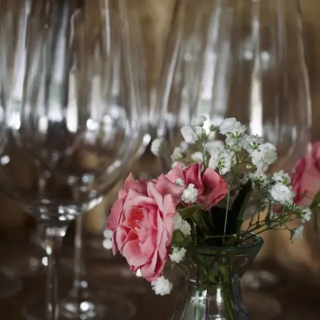 Un jarrón con rosas rosadas y aliento de bebé frente a copas de vino.