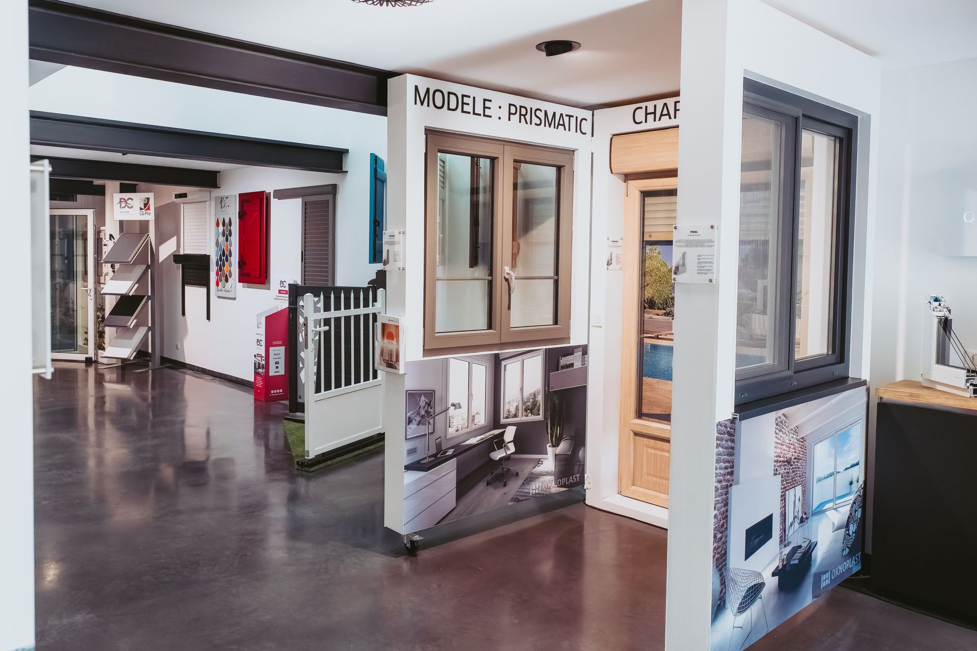 Une salle d'exposition présentant différents modèles de fenêtres et de portes, notamment des cadres en bois et gris, sur des murs blancs.
