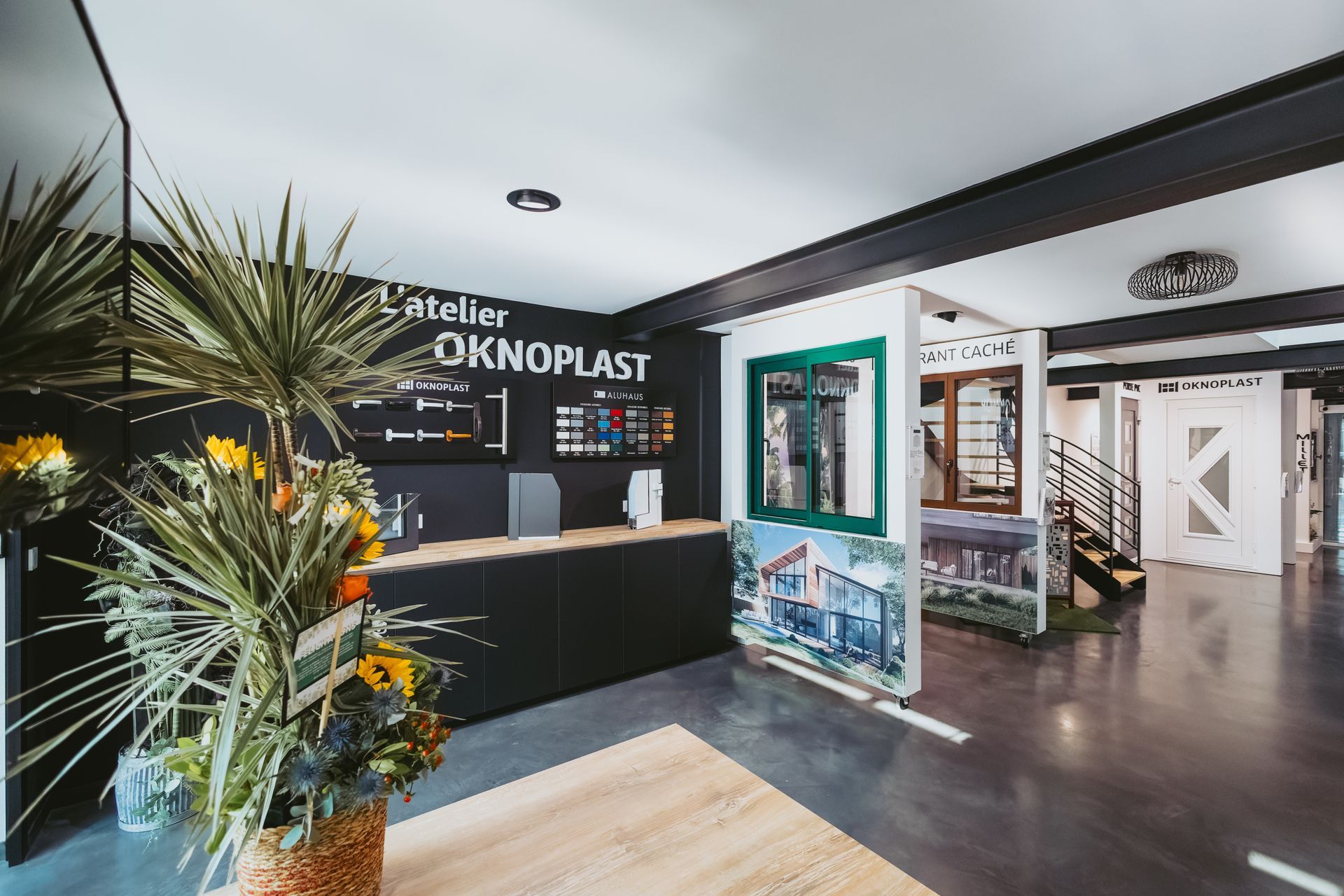 Un showroom Oknoplast moderne présentant des produits exposés, des vitrines et des échantillons de couleurs sur un mur noir.