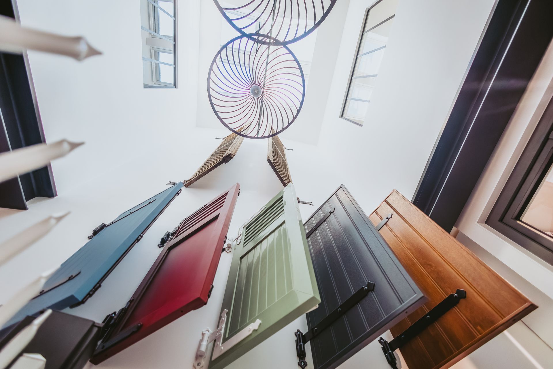 Cinq volets colorés sont suspendus dans un espace intérieur, sous des œuvres d'art décoratives circulaires et des puits de lumière.