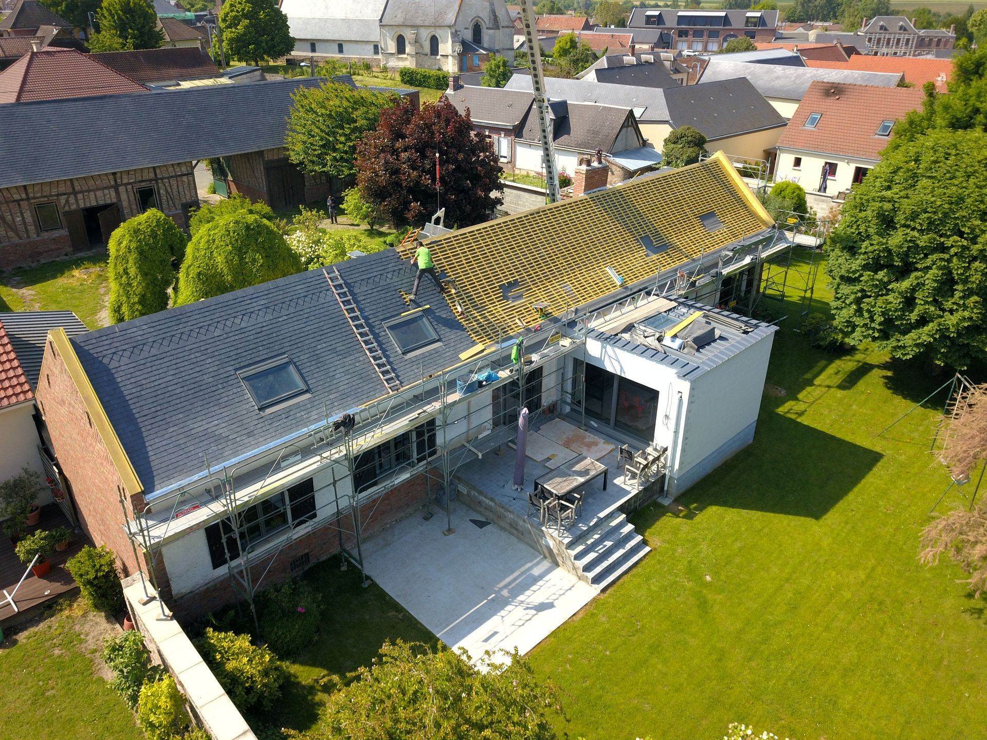 Vue aérienne d'une maison en rénovation avec un toit en ardoise et en bois partiellement terminé, dans un cadre suburbain.