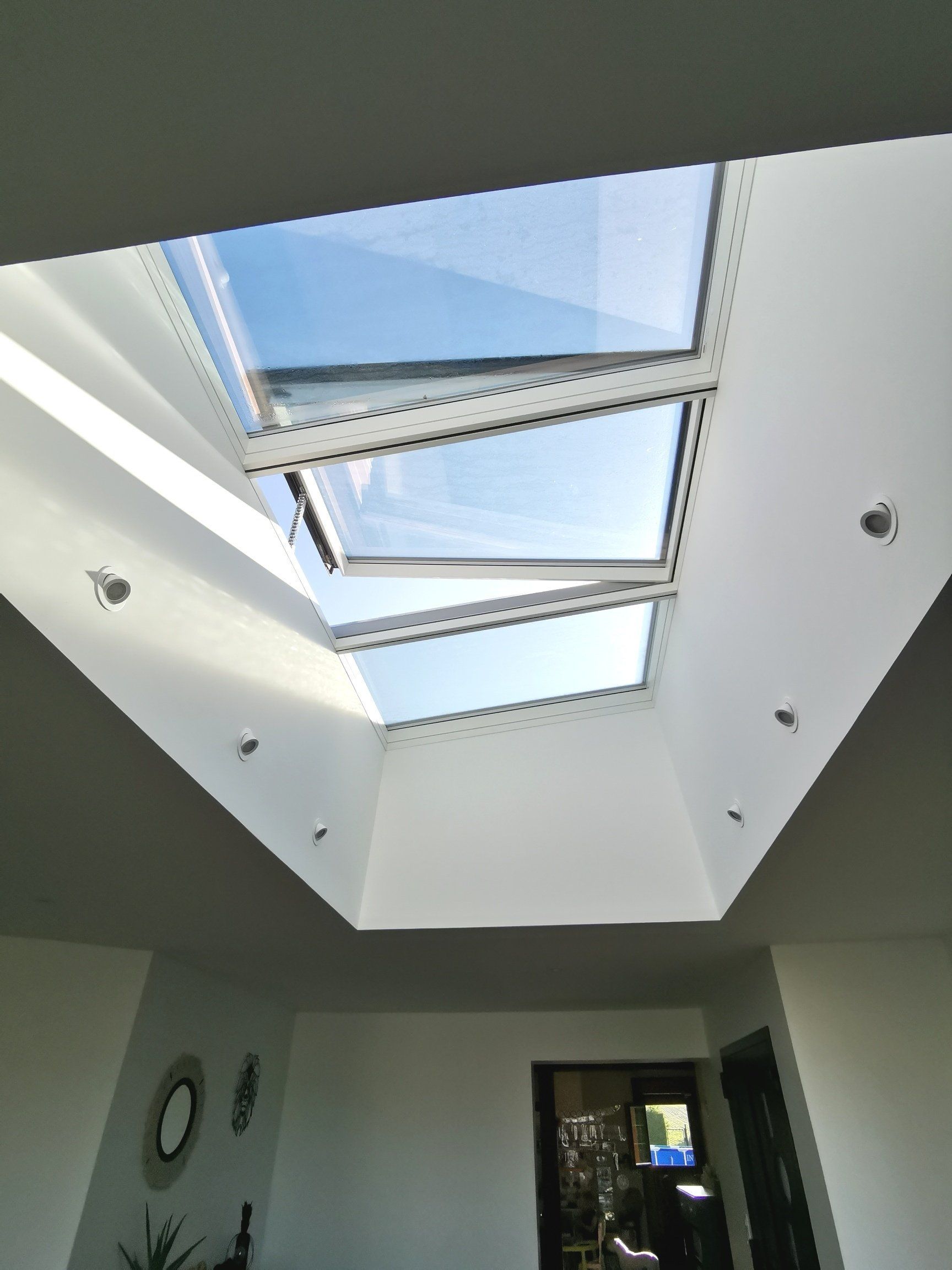 Vue plongeante sur une verrière intérieure moderne à sections encadrées de blanc, encastrée dans un plafond blanc.